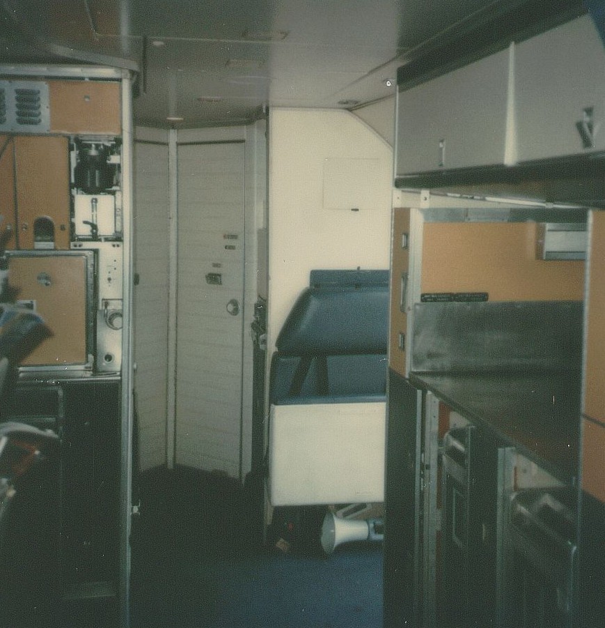 May 1979 The rear service area of a Pan Am Boeing 707.  In the far back are lavatory doors.  In the middle on the right is a folding crew jumpseat by the rear passenger door.  In the forward rigth is an auxiliary galley placed across from the main rear galley which can be partially seen in the forward left.  The auxiliary galley was needed for  the all charter configuration which featured 180 economy seats.